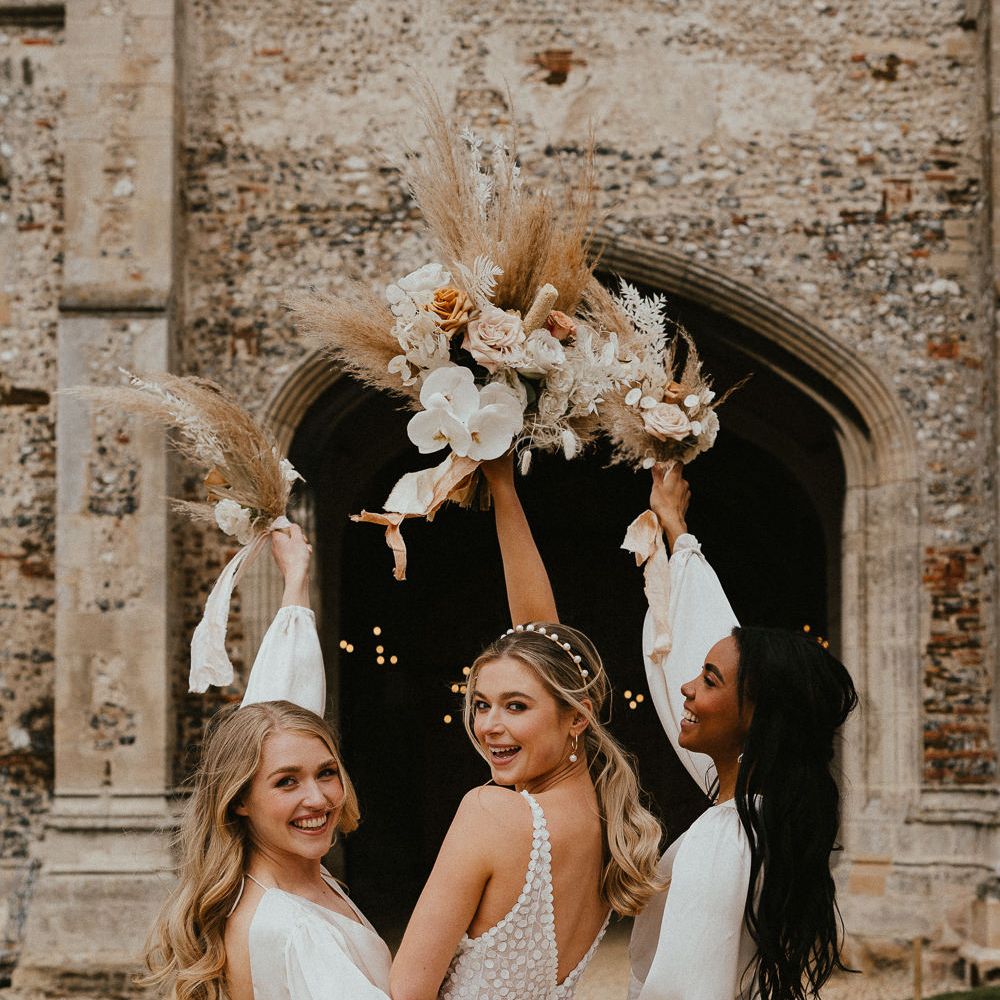 Bridal party portrait with bride and bridesmaids holding their neutral dried and fresh flower bouquets in the air 