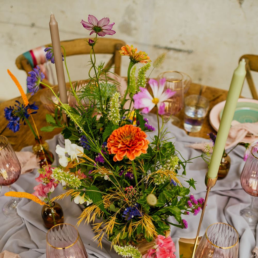 Fiesta theme wedding table decor with colourful wildflower centrepiece, taper candles, linens and coloured glassware 