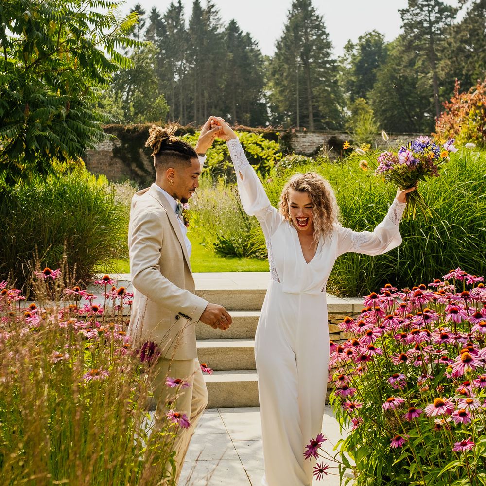 Groom in a beige suit twirling his bride in a jumpsuit in the Walled Gardens at The Fig House, Middleton Lodge 