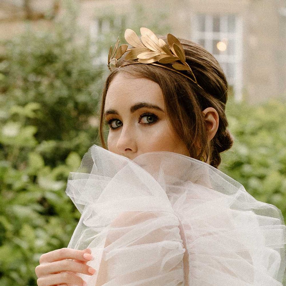 Beautiful bride with black eyeliner looking through her tulle puff sleeves wearing a gold headdress 