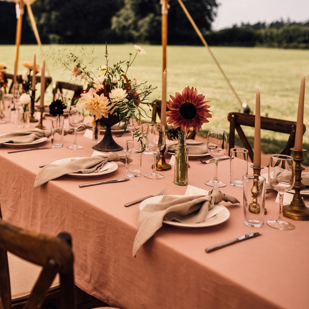 Two long wooden tables with dusky pink tablecloths, candles and assorted florals for marquee garden wedding reception in Cornwall