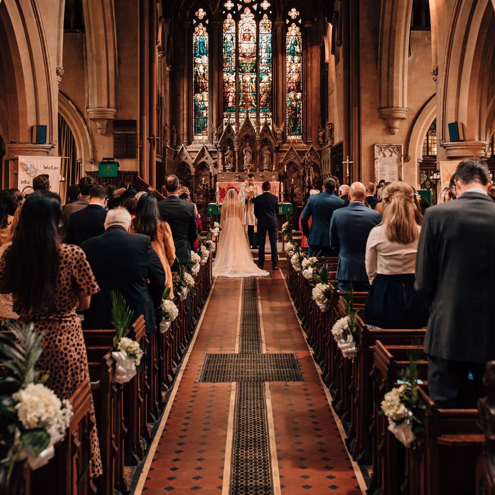 Interior or church with bride in white dress with train and groom in blue checked suit standing at the altar during church wedding ceremony