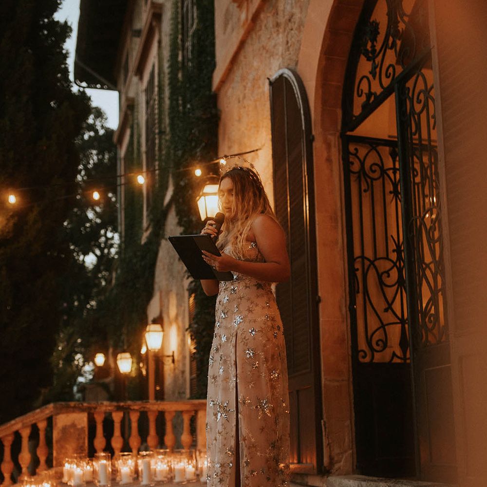 Bride gives speech on balcony on her wedding day as candles are lined around her