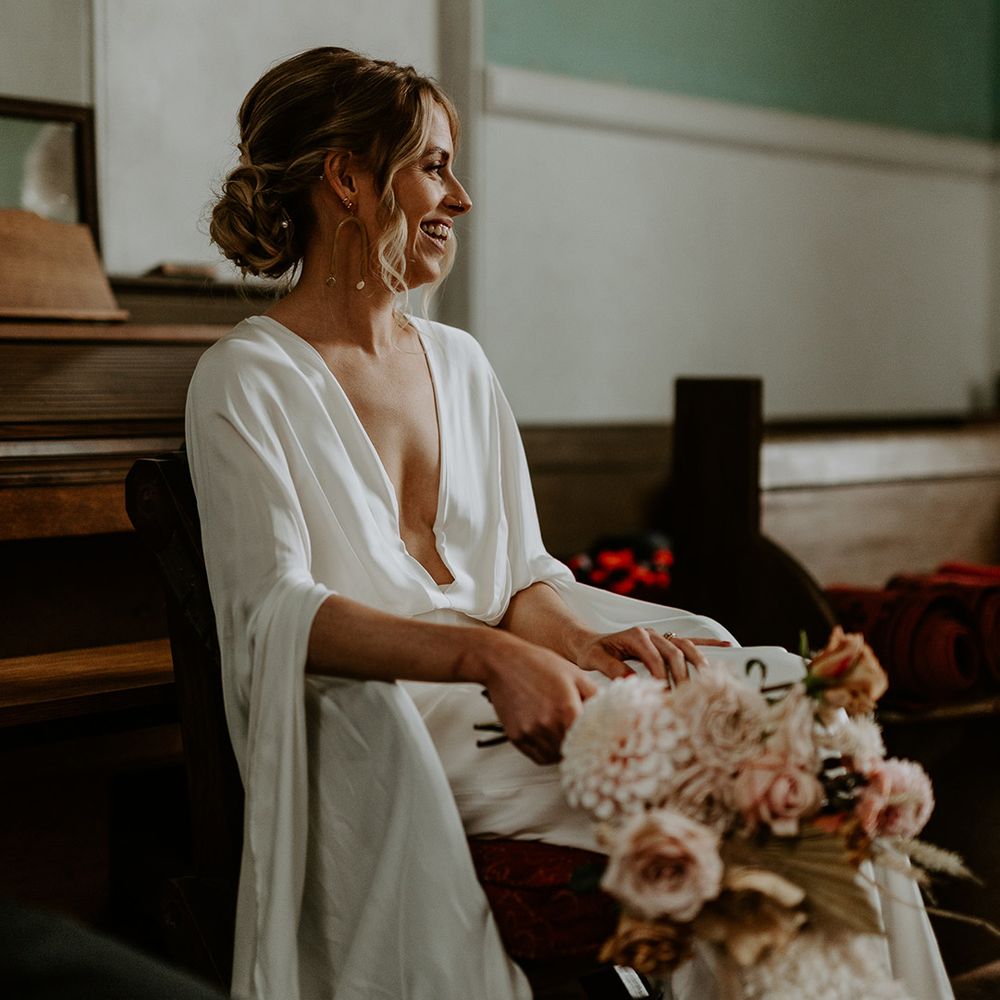 Bride sits down in church whilst holding boho floral bouquet