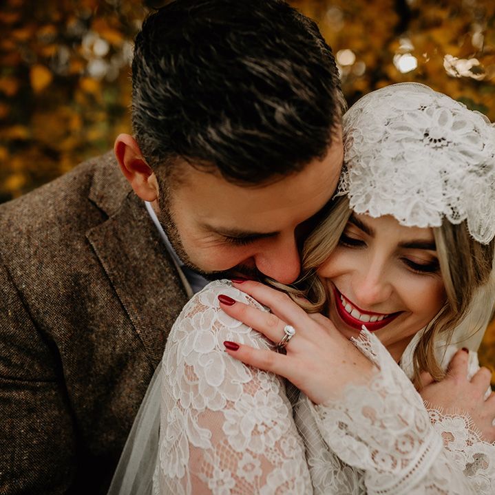 Groom nuzzling his bride's neck in a Juliet cap veil with bright red lipstick and nails 