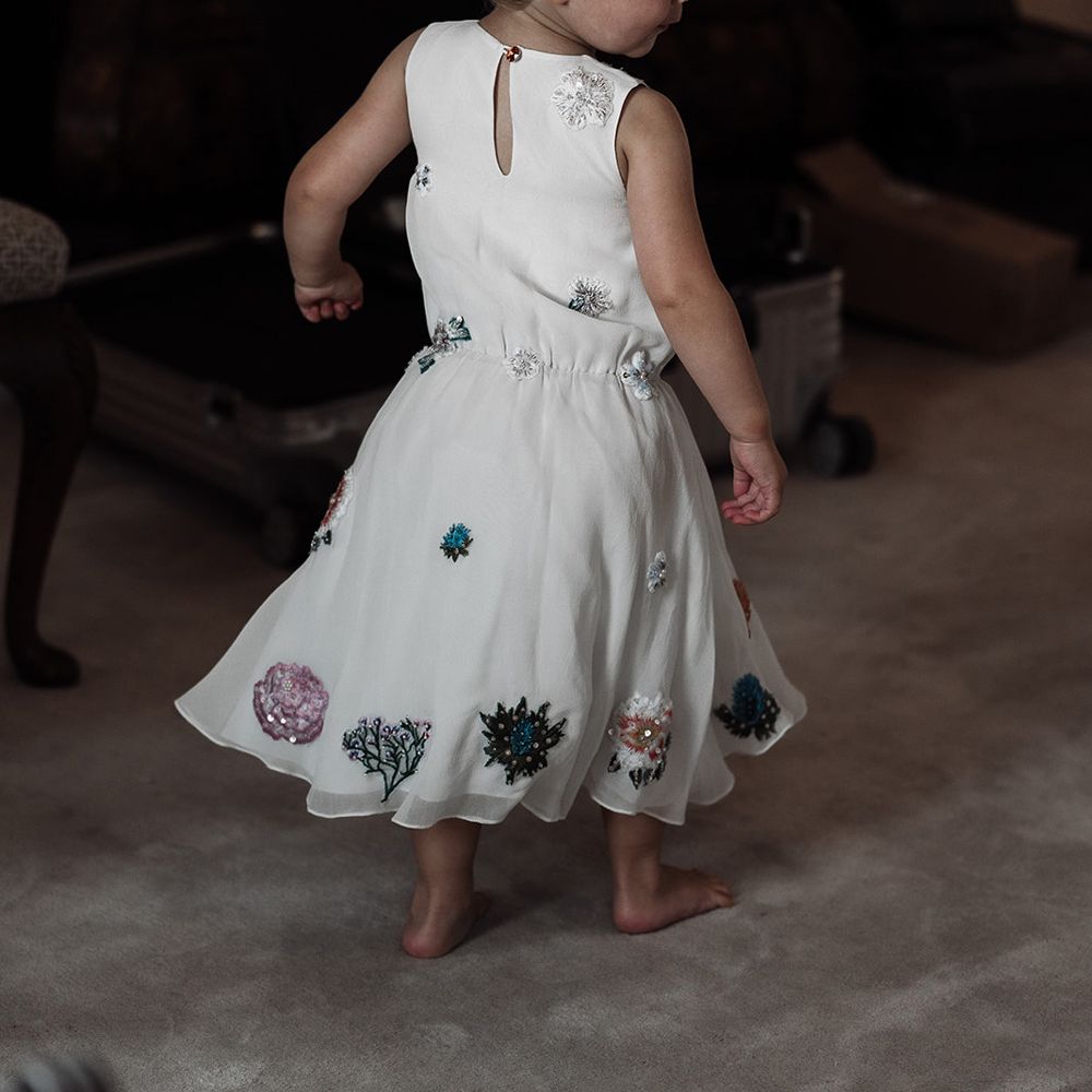 Flower girl in white dress with floral embroidery stands in bedroom before wedding