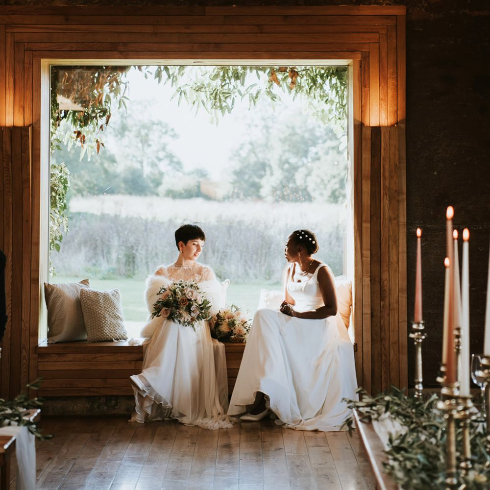 Bride in a Anna Kara wedding dress and faux fur stole sitting on a bench with her Black bride in a Essense of Australia wedding dress 
