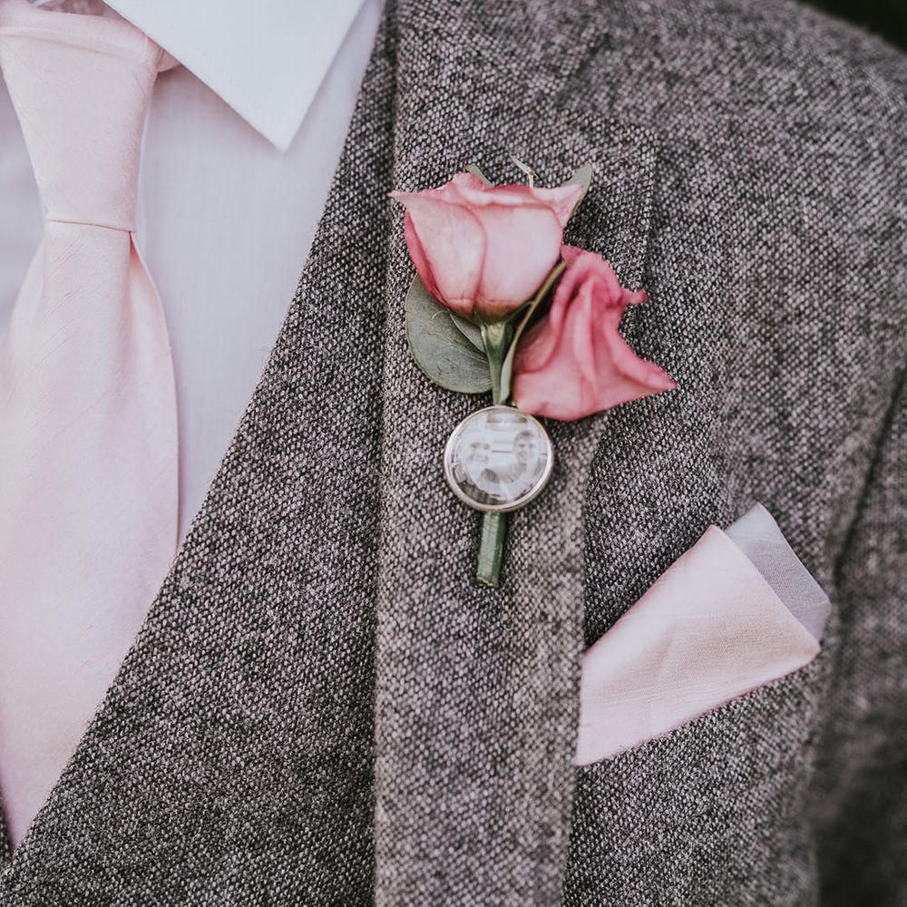 Grey tweed suit with pink rose buttonhole and personalised pin of groom and lost family member 