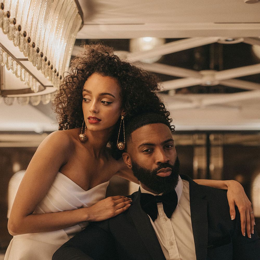 Black bride in a. strapless wedding dress with naturally curly hair, red lipstick and dangly earrings embracing her groom in a tuxedo at Mayfair Townhouse 