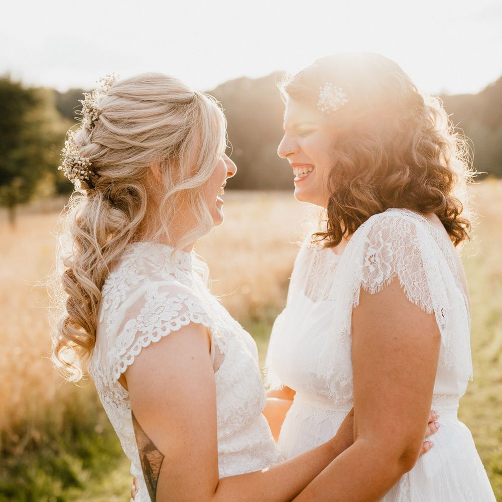 Brides laugh together at golden hour in white wedding dresses with sheer high neck design