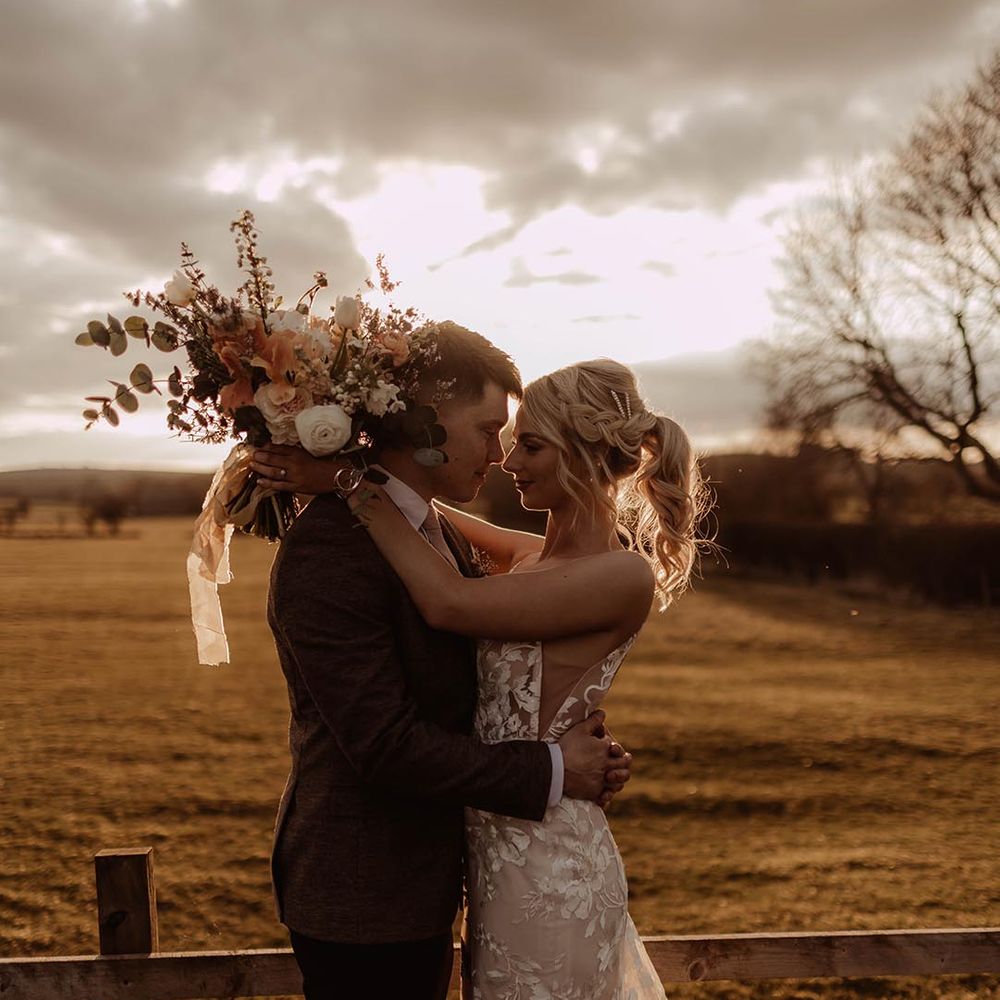 Bride with blonde braided ponytail hairstyle with diamanté clip in Made With Love wedding dress with groom in three piece brown suit