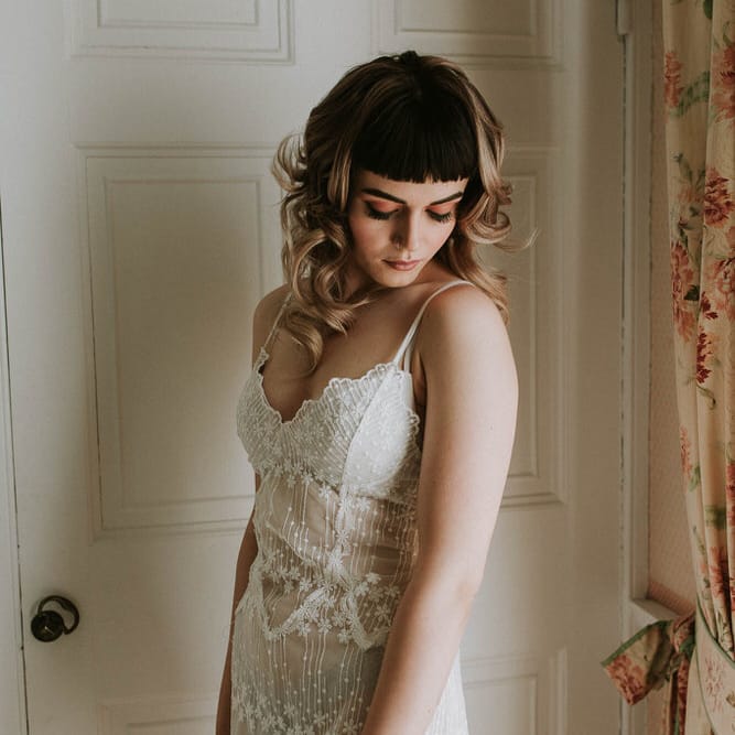 Bride with a blunt fringe and curly hair wearing a teddy wedding lingerie on wedding morning