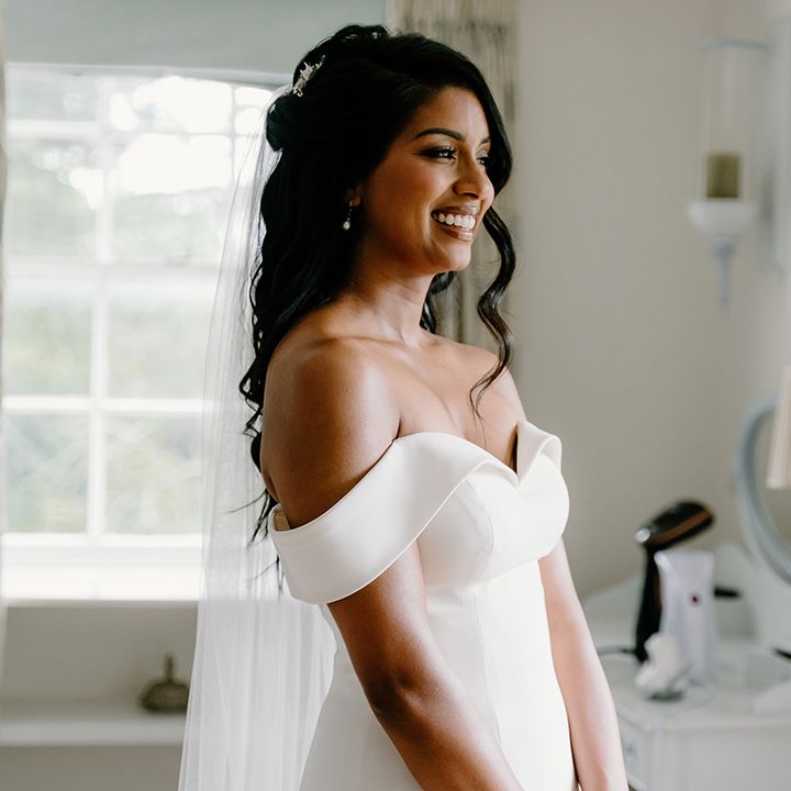 Bride with half up half down styled hair in an off the shoulder wedding dress with pearl earrings and sparkly hair accessories 