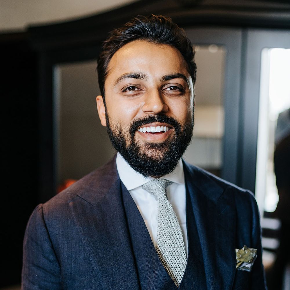 Groom wears three piece blue suit with textured grey tie and floral buttonhole 