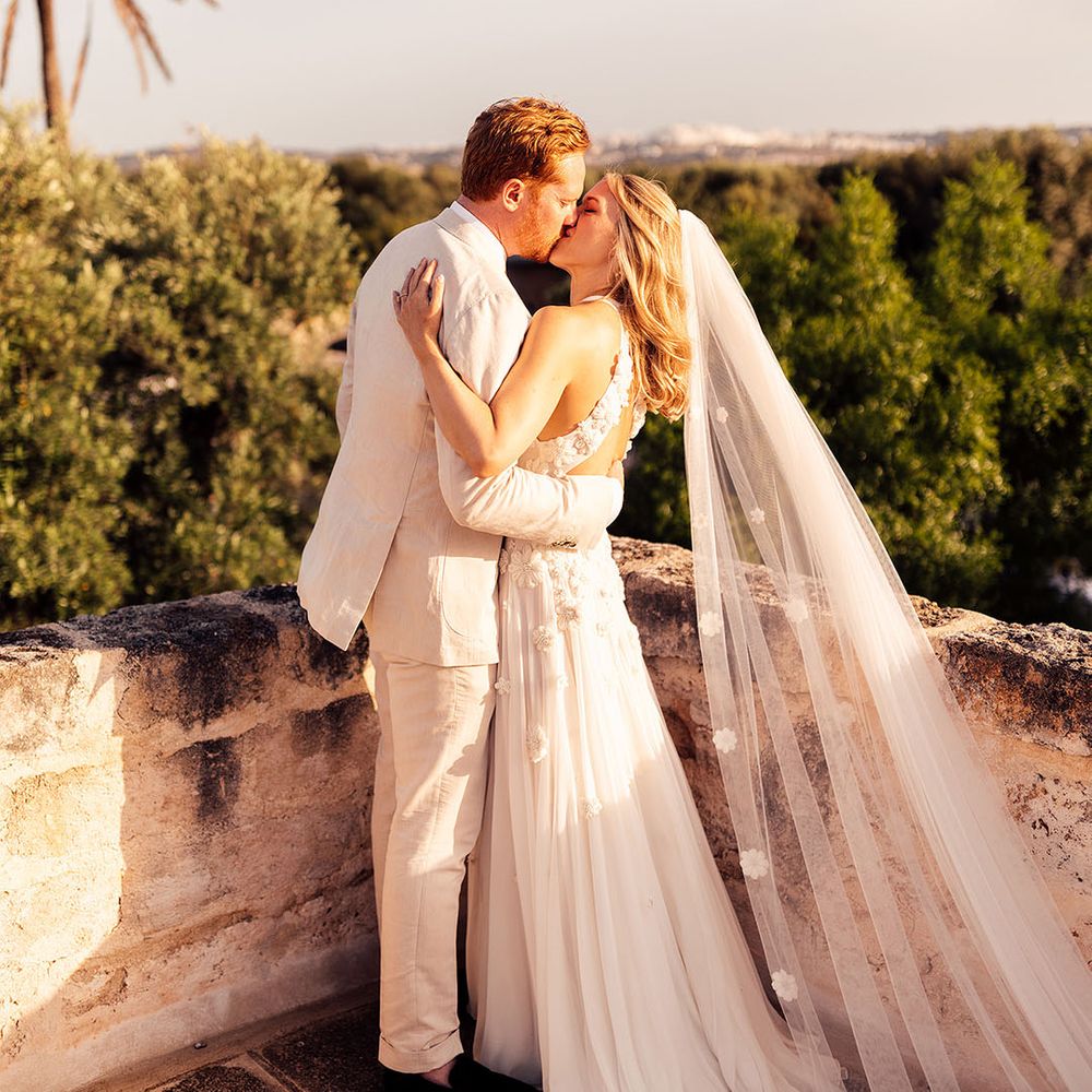 Groom in a cream wedding suit kisses the bride in a flower wedding dress and matching flower veil 