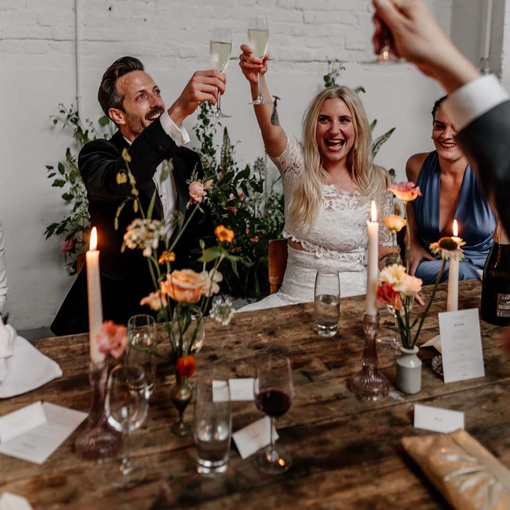 Bride in boho two piece lace bridal outfit and groom in dark tux with bowtie cheering at wedding reception