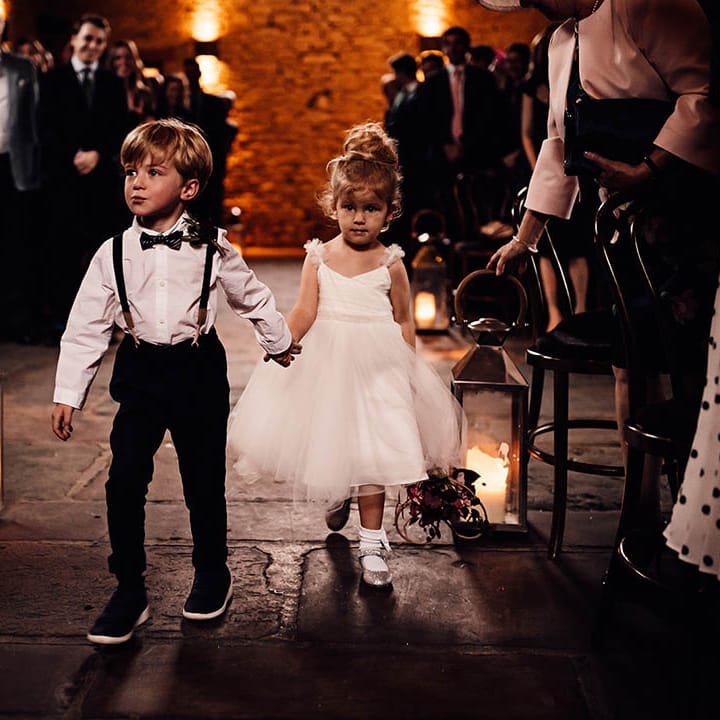 Adorable page boy and flower girl walk down the aisle together holding hands