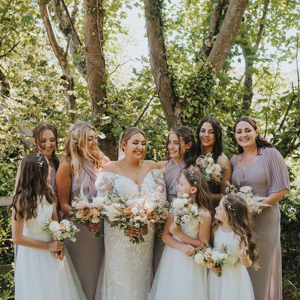 Bride stands with her bridesmaids in pink bridesmaid dresses with mismatched styling holding floral bouquets 