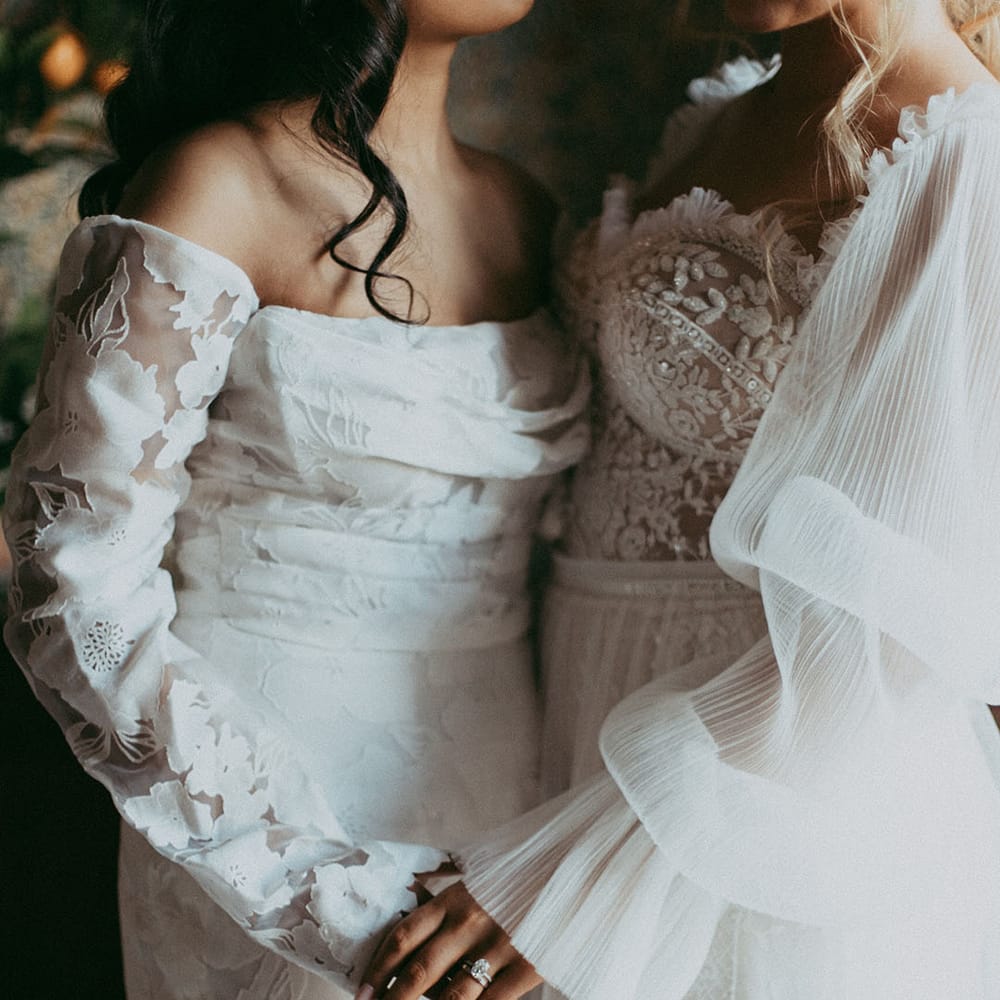 Brides wearing off shoulder long sleeve wedding dress and lace detailed wedding dress with puff sleeves holding hands