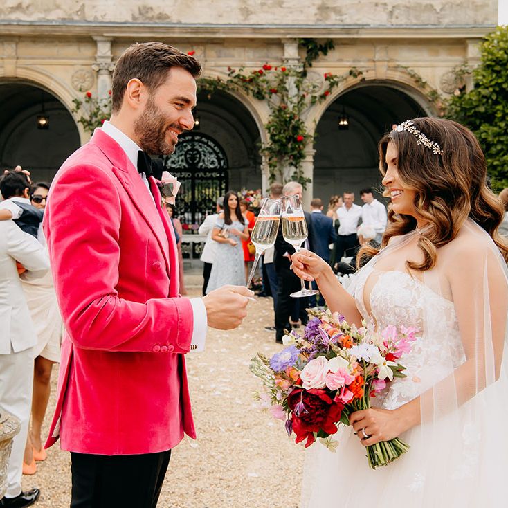 The bride in a strapless gown and groom in a bright pink velvet suit jacket share a cheers together after their ceremony 