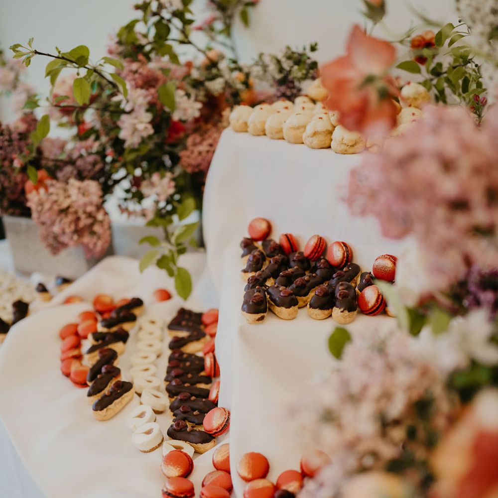 Dessert table complete with mini eclairs and colourful macaroons surrounded by bright florals 