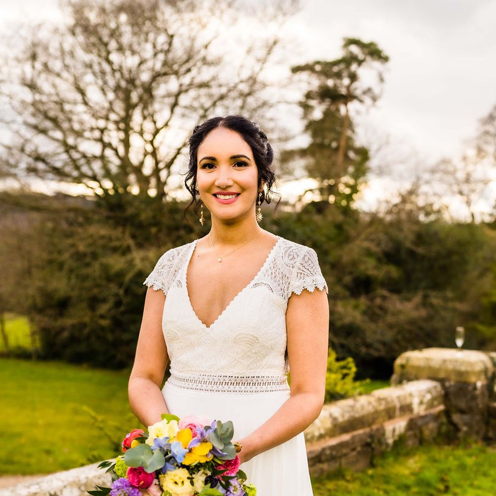 Bride holds waterfall styled bridal bouquet complete with Spring flowers in vibrant colours 