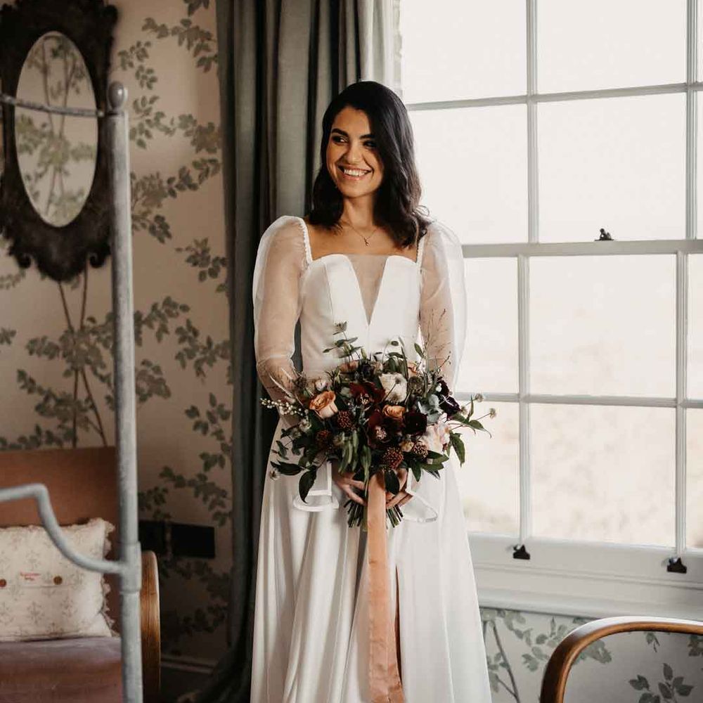 Bride in sheer puff sleeve wedding dress with front slit holding large neutral bouquet with mustard velvet ribbon 