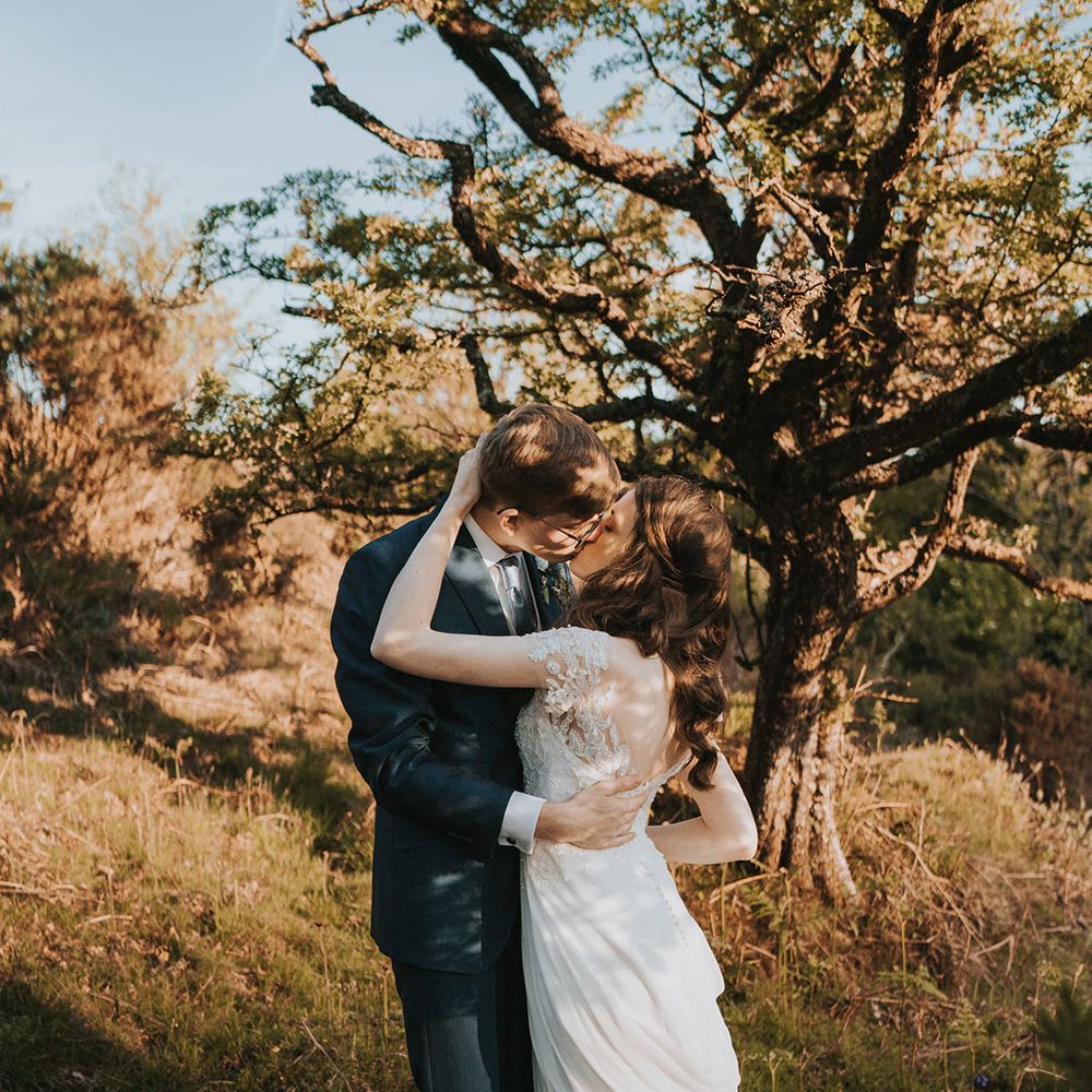 The bride in a lace short sleeve wedding dress kissing the groom passionately who wears a navy wedding suit 