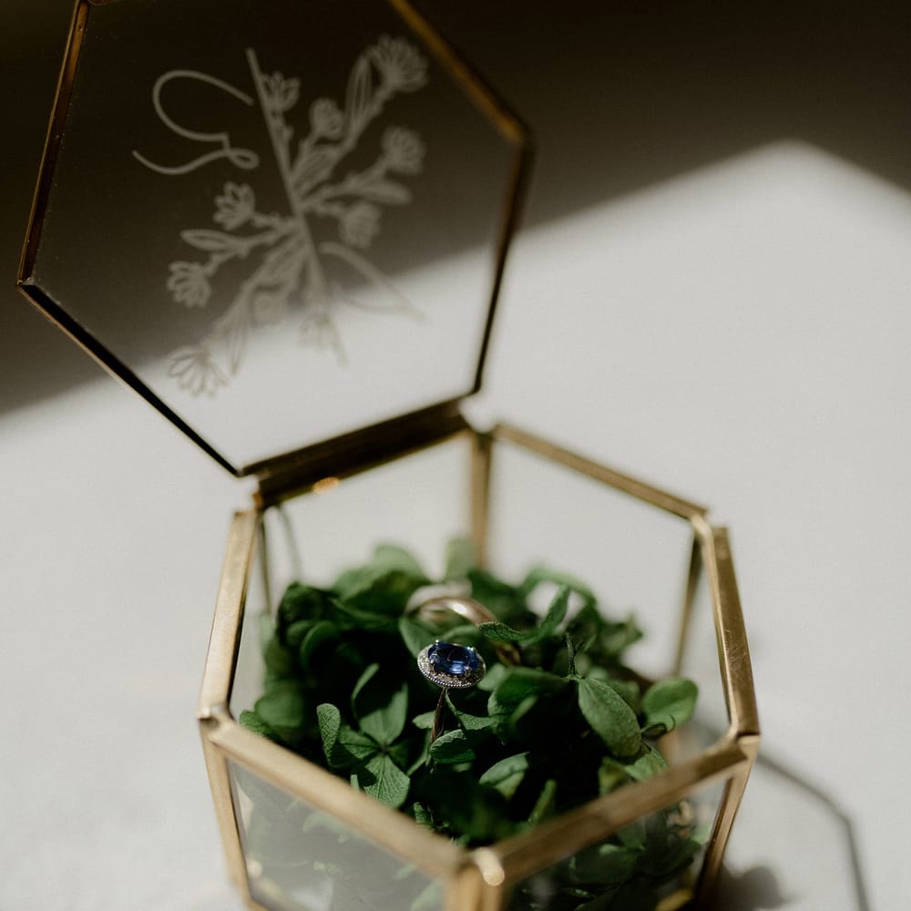Blue engagement ring in clear and gold ring box with greenery