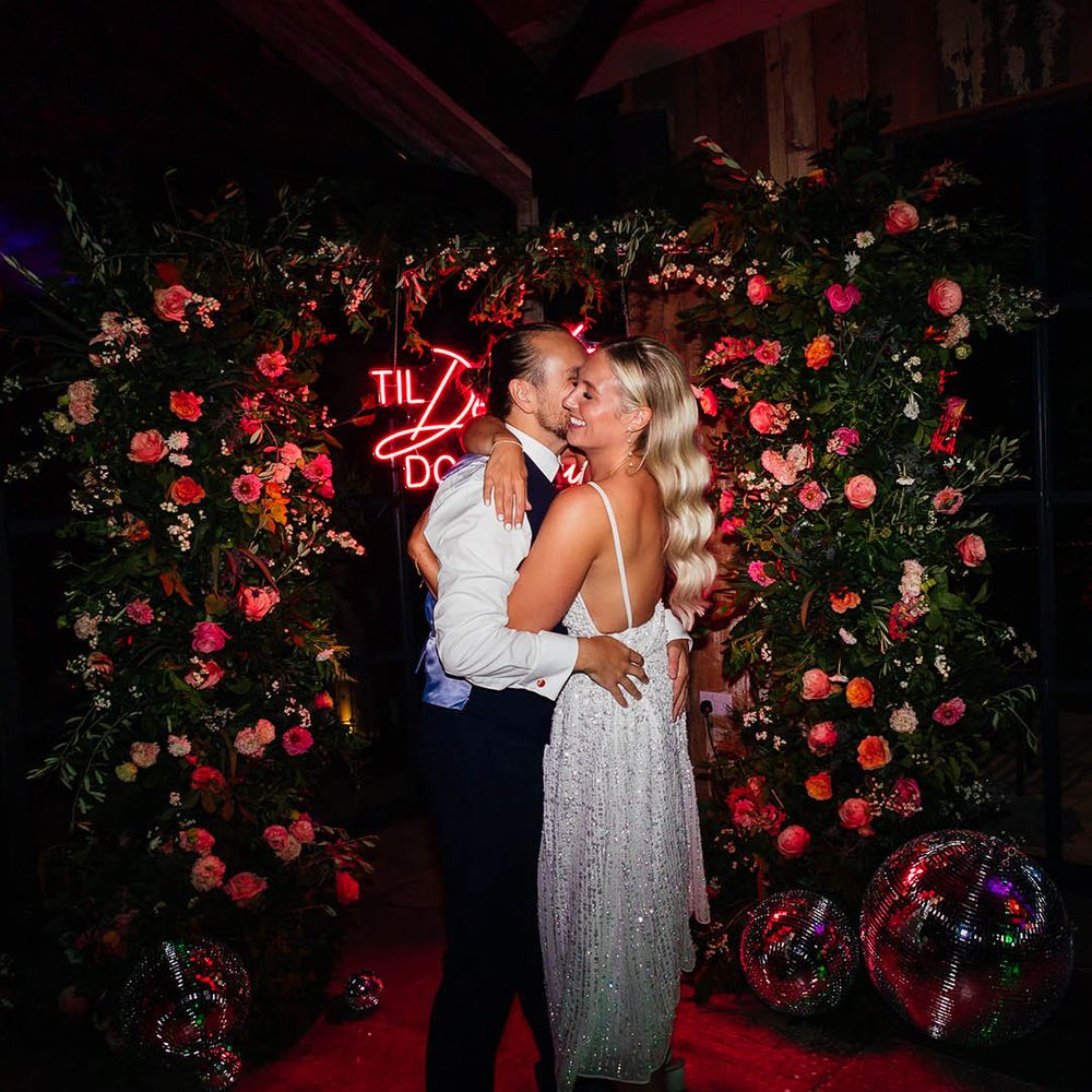 Bride in short sparkly reception dress with the groom in front of red neon wedding sign