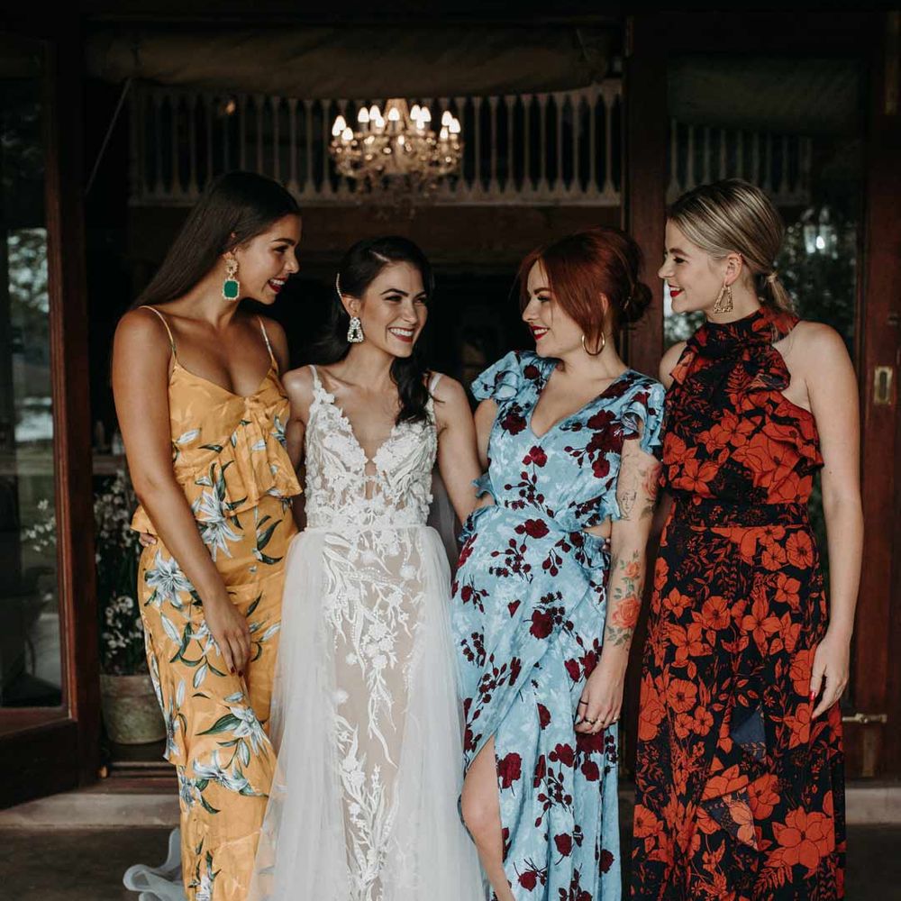 Bride in sleeveless lace and tulle wedding dress standing with bridesmaids in mismatched colourful floral patterned bridesmaid dresses 
