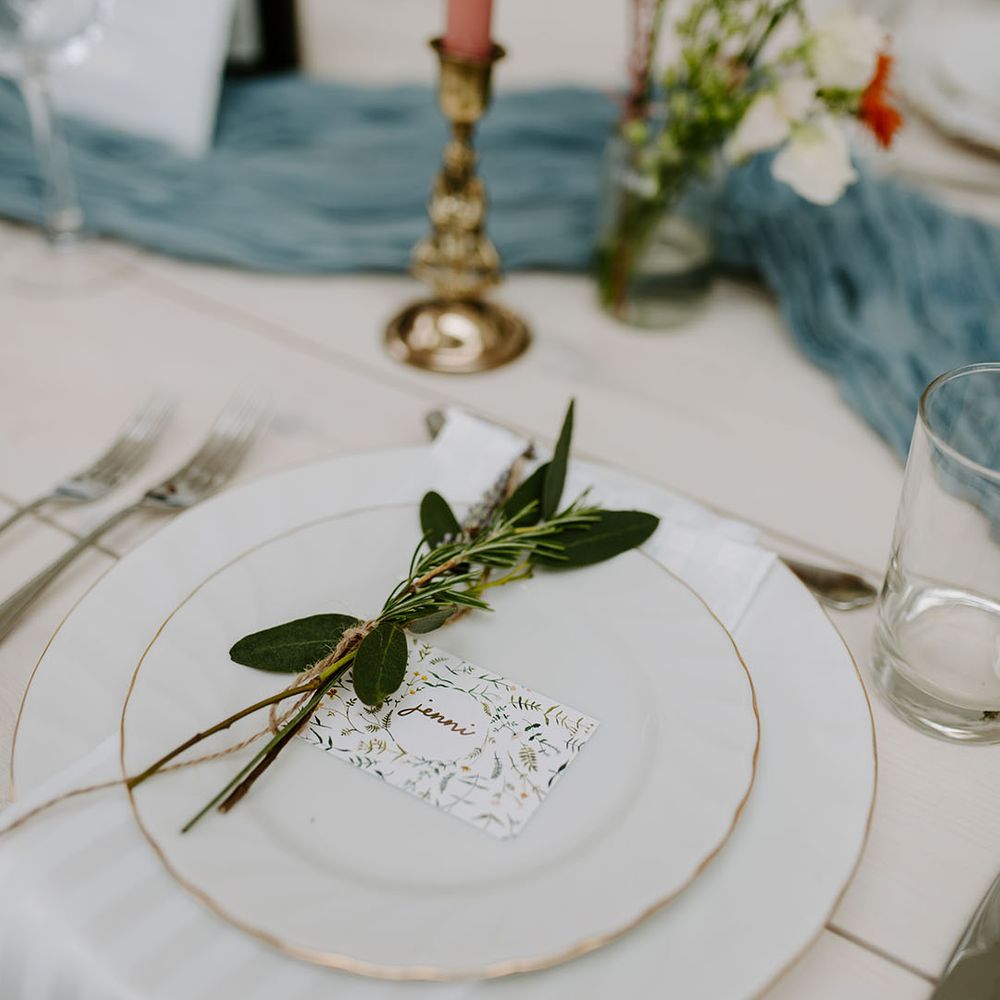 Wedding place setting with white plates, DIY wedding place name and sprig of herbs 