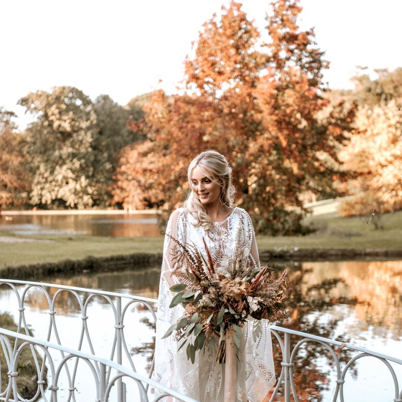 The bride holds her pampas grass bouquet standing on a bridge over the lake