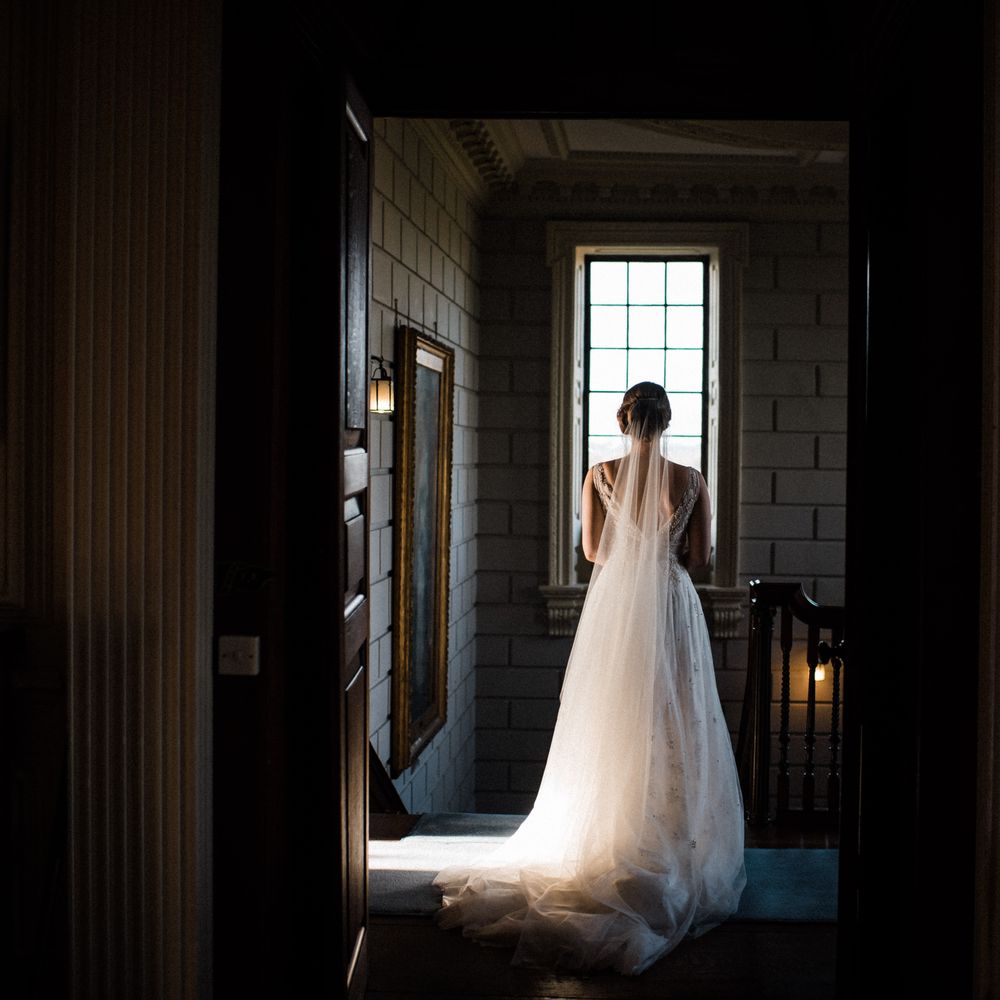 Bride stands in front of the window on the morning of her wedding