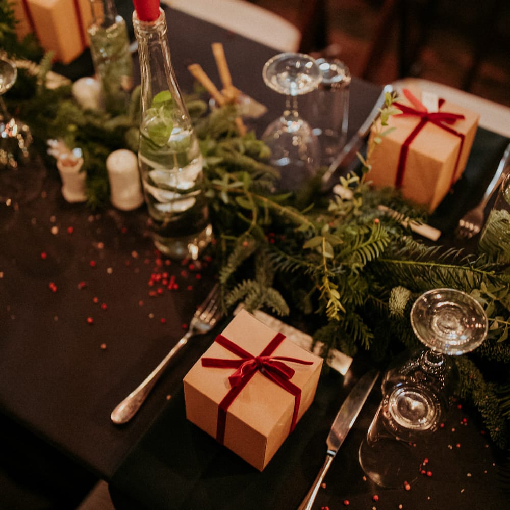 Christmas wedding table decor with pine leaves centrepieces, and brown favour boxes tied with red ribbon