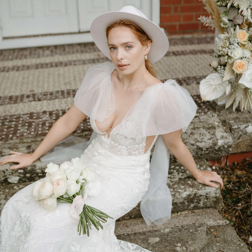 Bride wearing a blush pink stetson hat, puffed tulle shoulder wedding dress with plunge neckline and natural makeup