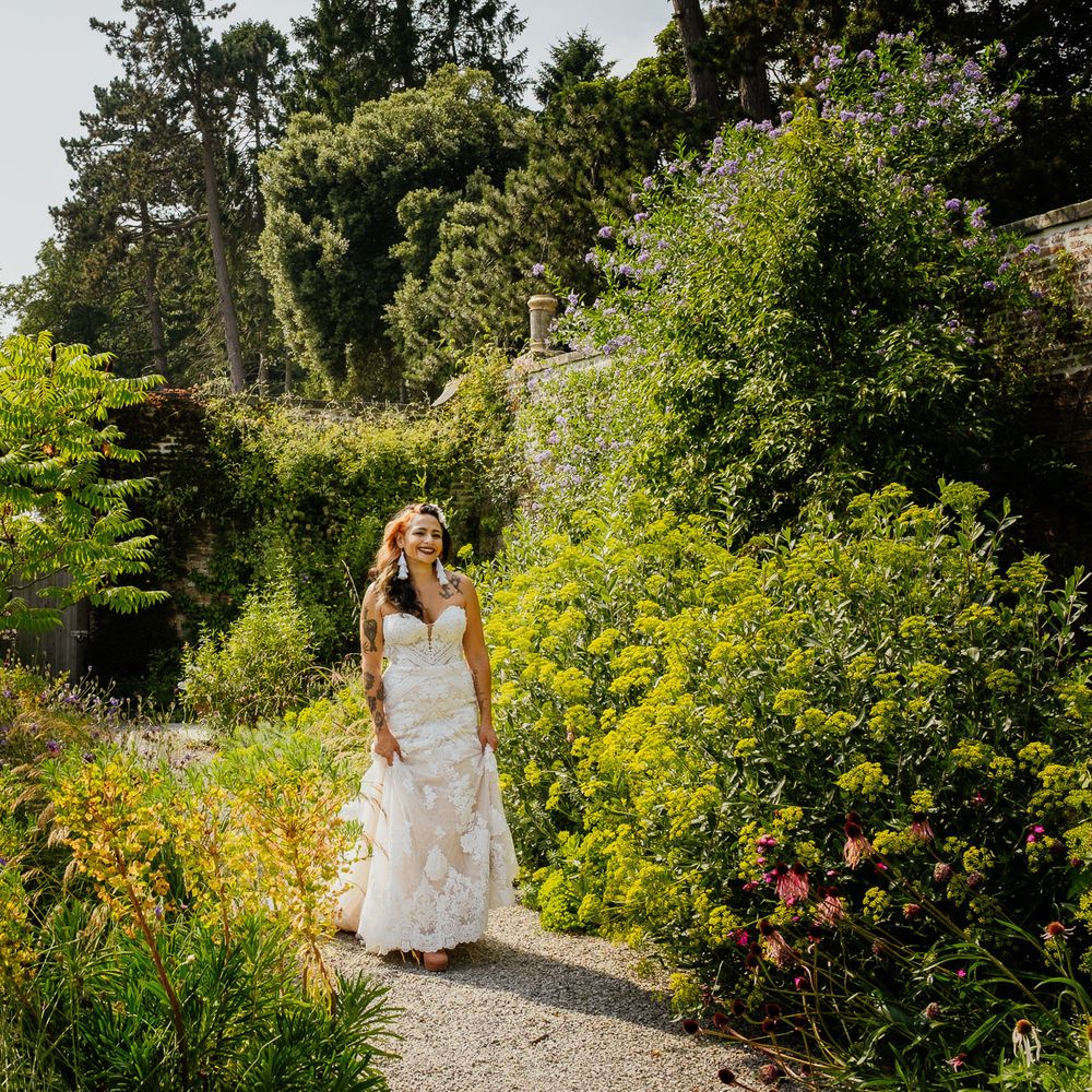Boho bride in a strapless lace wedding dress and tassel earrings walking through the Walled Gardens at The Fig House, Middleton Lodge 