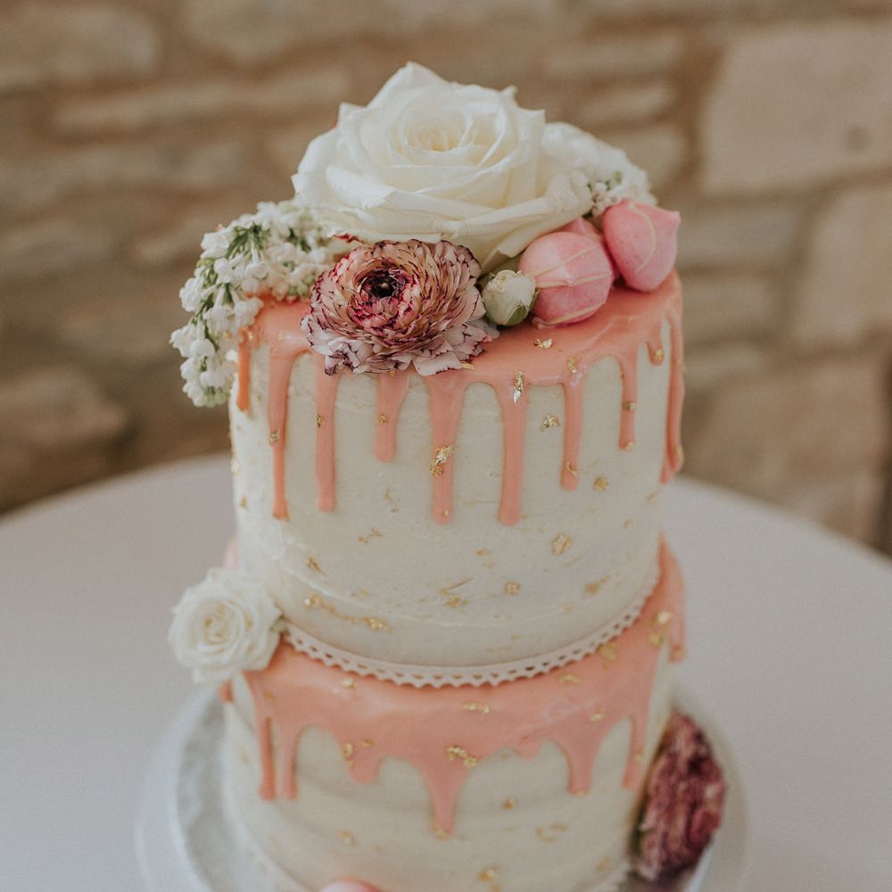 Two tier wedding cake with buttercream frosting, pink drip icing, meringue kisses and rose decor 