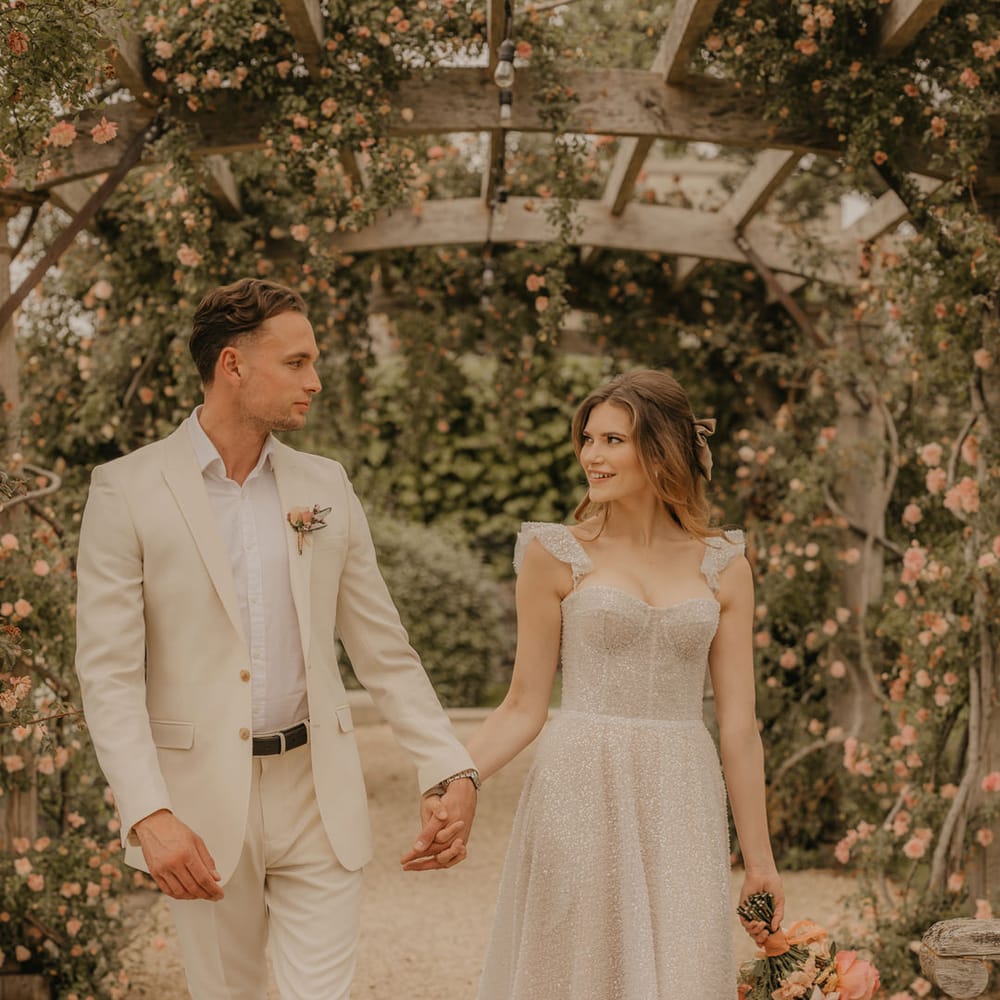 Bride and groom portrait under the pergola at Euridge Manor with groom in a stone suit and brown loafers and bride a sparkly Made With Love wedding dress