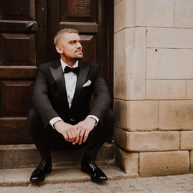 Stylish groom sitting on a step in a Reiss tuxedo with satin lapels, bow tie and shiny shoes 