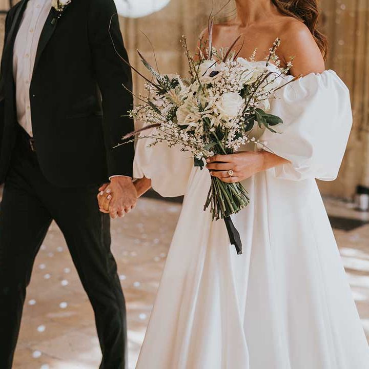 Bride in a strapless wedding dress with detachable puff sleeves holding a white wedding bouquet with roses, astilbe and anemones 