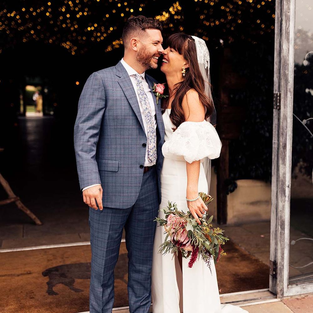Bride & groom embrace and laugh with one another as bride holds colourful floral bouquet and wears Rime Arodaky dress complete with Miu Miu platform sandals