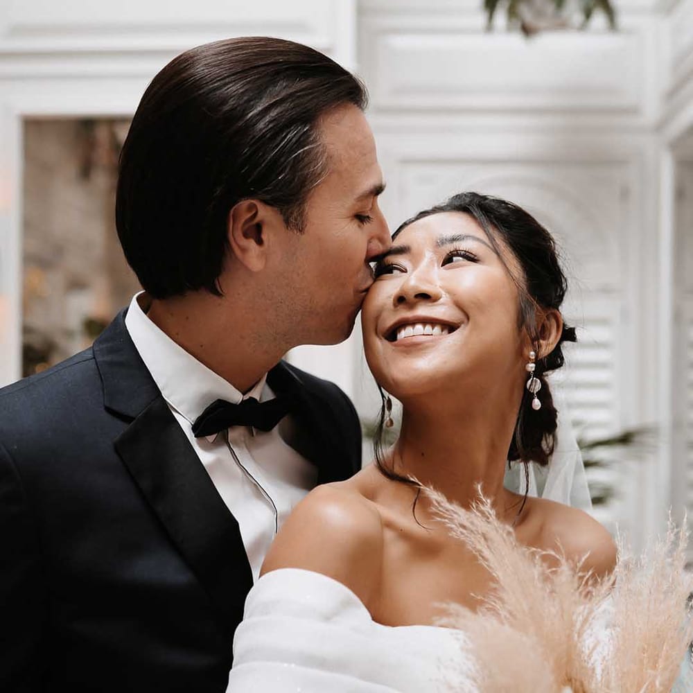 Groom kisses Bride with long pearl earrings and sparkly off the shoulder sleeve