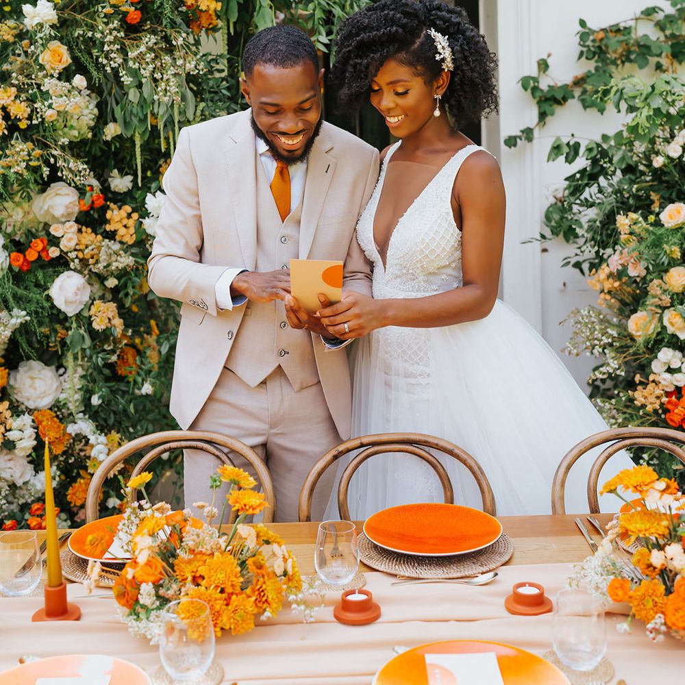 Bride in a plunging neckline wedding dress reading the wedding menu with her groom at their orange decorated outdoor reception 