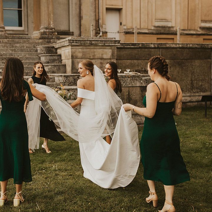 Bride has help from bridesmaids as they hold her bridal gown on wedding day
