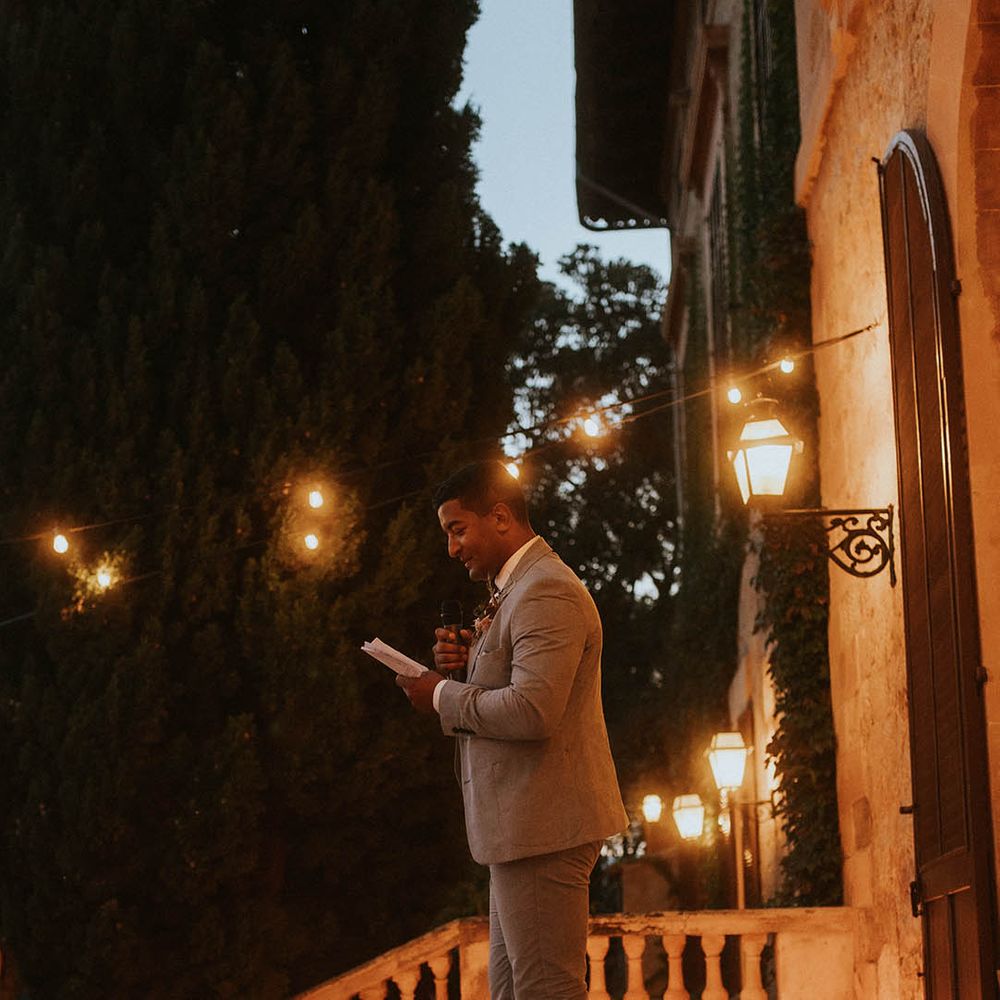 Groom stands outdoors on balcony with candles 