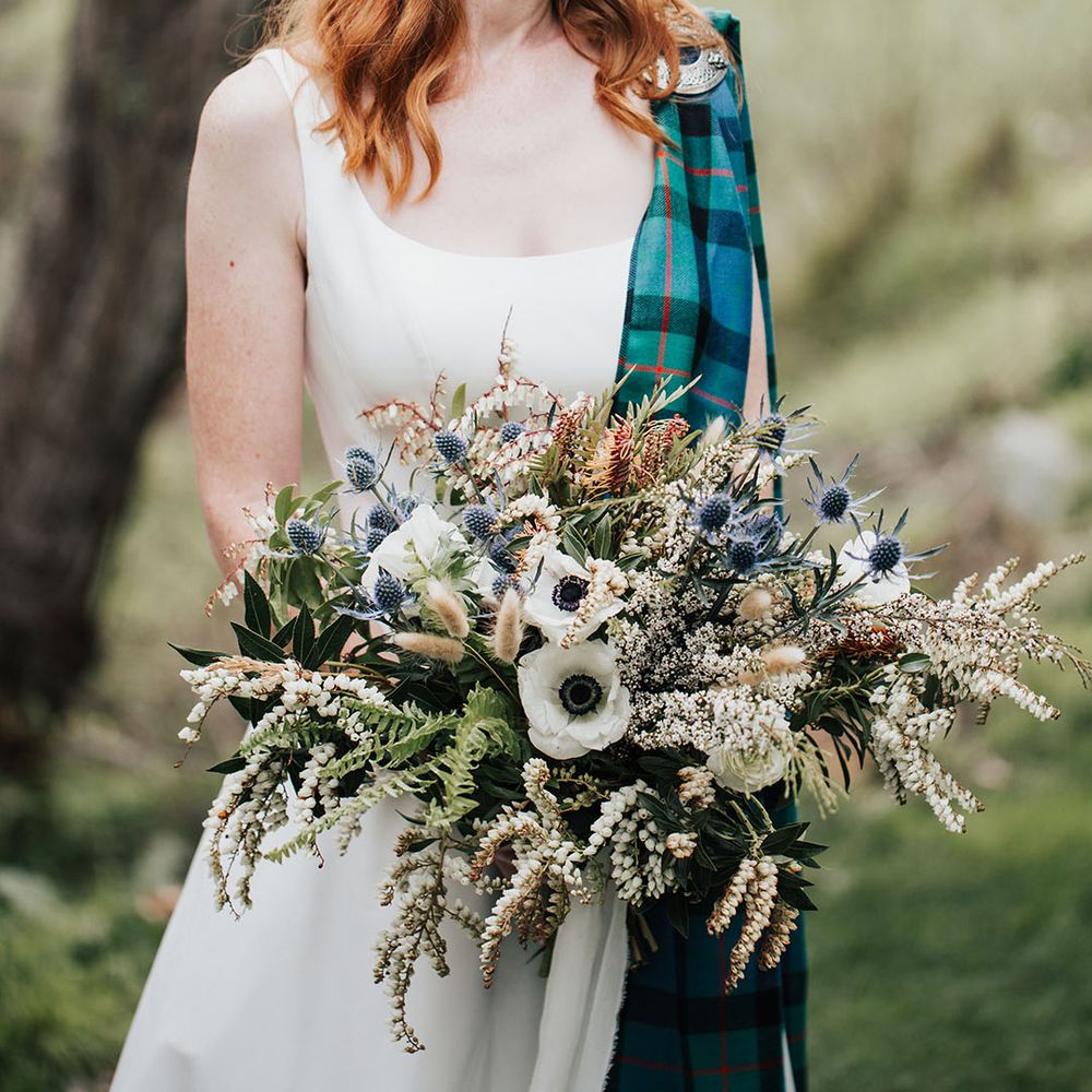 beautiful bride with red hair with hair up half down braided hairstyle holding an anemone, thistle and wildflower wedding bouquet 