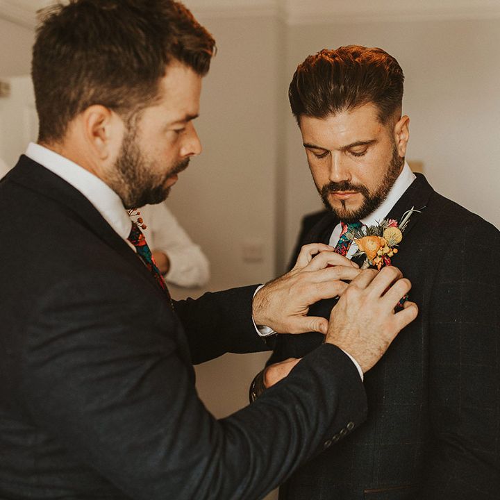 Best man putting on the grooms colourful flower buttonhole flower 