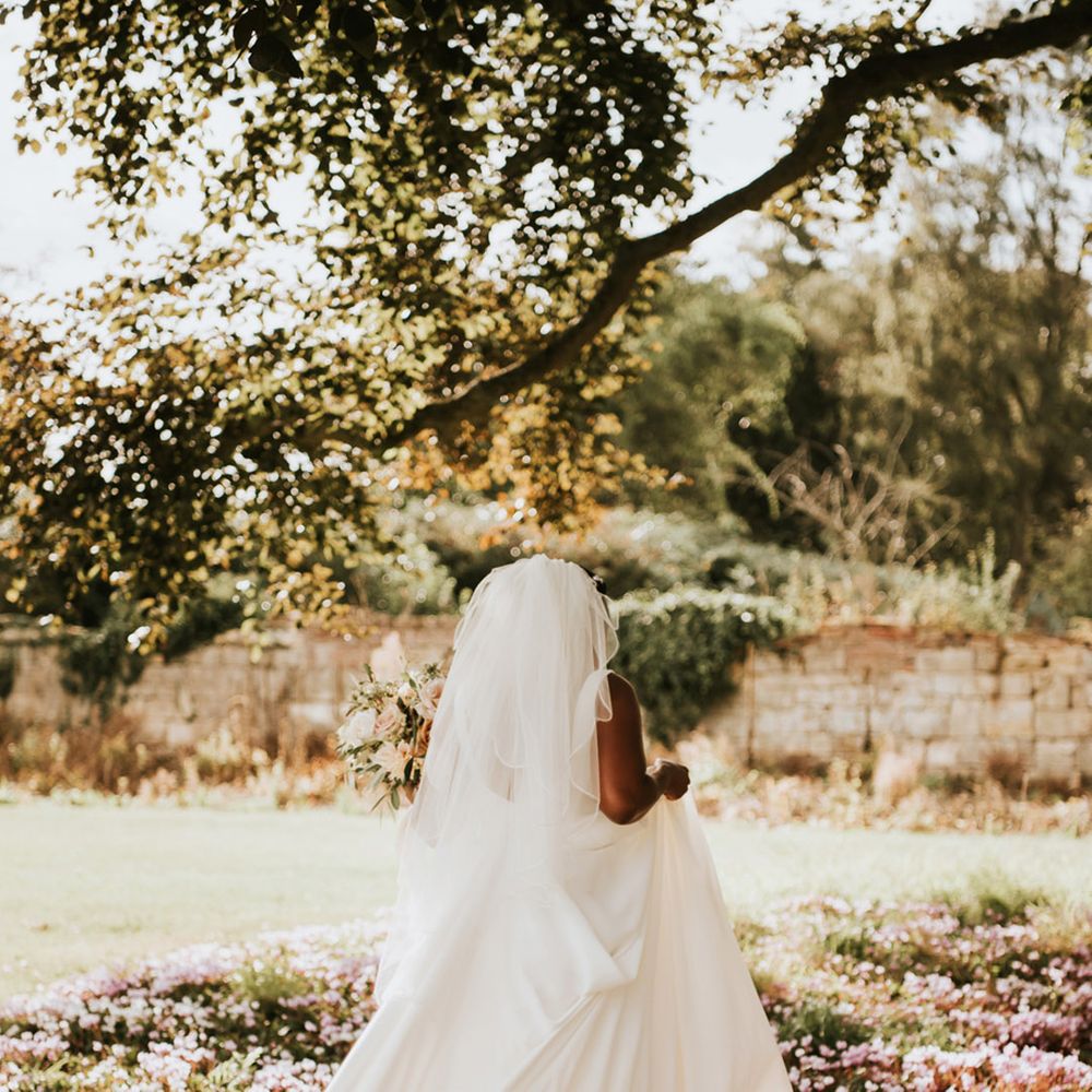Black bride in an Essense of Australia wedding dress and cathedral length veil walking through the flower bed 