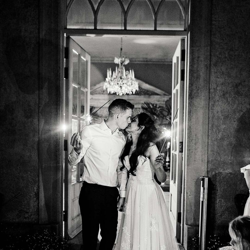 Bride & groom kiss as they hold sparklers in black & white image